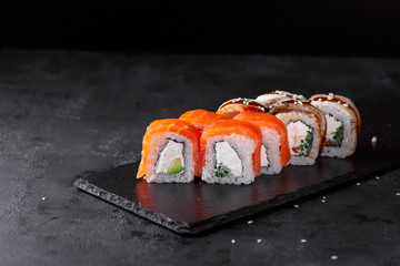 Sushi rolls with creamy cheese, cucumber, salmon, eel, rice, nori on a black background