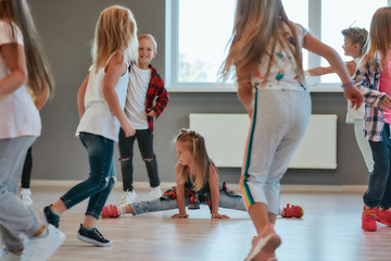 Gymnastic exercises. Little cute girl sitting on a twine while having a choreography class. Group of positive and active children learning a modern dance in the dance school