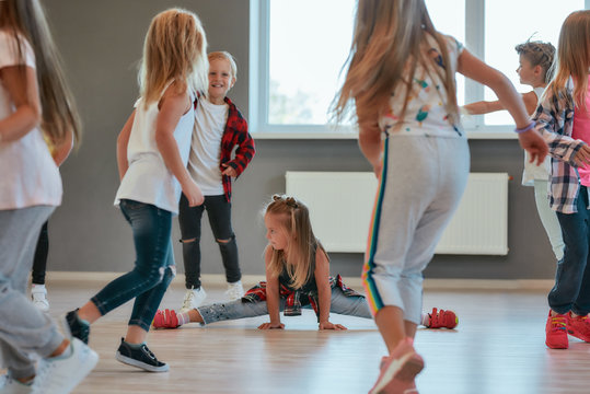 Gymnastic Exercises. Little Cute Girl Sitting On A Twine While Having A Choreography Class. Group Of Positive And Active Children Learning A Modern Dance In The Dance School