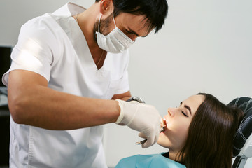 Obraz na płótnie Canvas Closeup young woman at dentist clinic office. Male doctor performing extraction procedure with forceps removing patient tooth. Doctor in disposable medical facial mask.