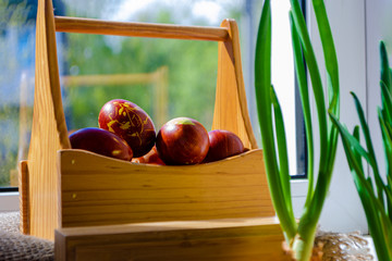 Easter eggs are coloured by the ancient onion husk method with various natural patterns in box by window in sunshine on beige burlap next to sprouted green onion. Concept of light Christian holiday