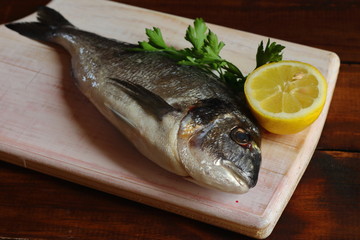 Composición plana con pescado dorada fresco, limón y perejil en tabla de madera