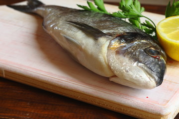 Composición plana con pescado dorada fresco, limón y perejil en tabla de madera