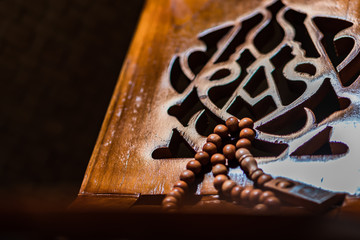 Islamic prayer beads or tasbih on rihal or quran book stand made from carved wood. It is suitable for background of Ramadan-themed design concepts or other Islamic religious events.