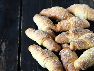 Croissants sprinkled with sesame and sugar on a dark wooden background.Homemade cake.