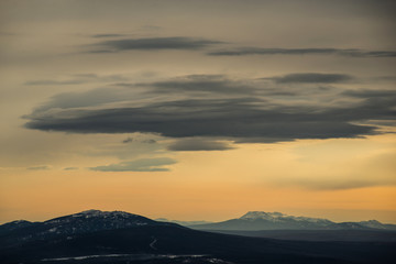 yellow sunset sky with large blue clouds against the background of mountains