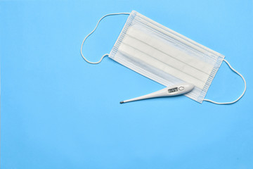 Medical thermometer and surgical mask on a blue background.