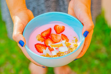 hand holding a dessert with yogurt, strawberry, coconut and cereal