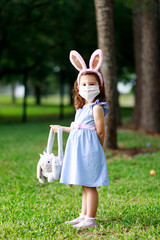 Little toddler girl with bunny ears and surgical face mask hunting for Easter eggs during coronavirus quarantine - 337055634
