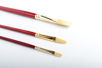 Three professional artist painting brushes displayed horizontally isolated on a white studio paper, photographed with soft focus
