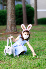 Little toddler girl with bunny ears and surgical face mask hunting for Easter eggs during coronavirus quarantine - 337056262