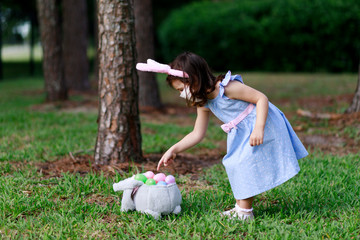 Little toddler girl with bunny ears and surgical face mask hunting for Easter eggs during coronavirus quarantine - 337056814