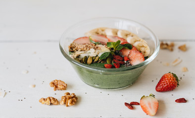 Smoothie bowl with banana and spirulina, almond flakes, chia seeds, pumpkin seeds and strawberry on white background.