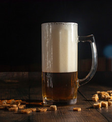 On a wooden table is a mug of cold foamy beer. Close-up. Black background.