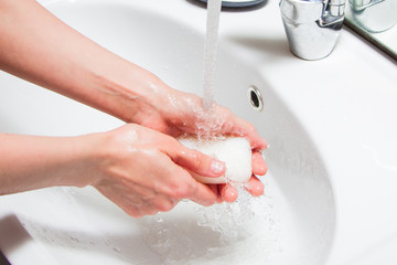 The girl washes her hands with soap under a stream of water