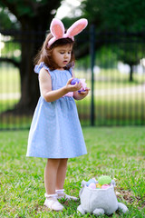 Little toddler girl with bunny ears. Easter egg hunt. - 337057811