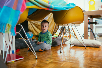 little boy playing in his built indoor fort in living room - obrazy, fototapety, plakaty