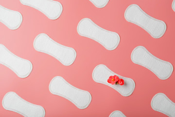 Sanitary pads on a pink background in the form of a diagonal pattern of repetitions, with a red flower on the pad.