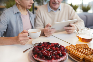 Close-up of fruit pie on the table served for breakfast with mature couple using tablet pc in the background