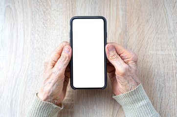 Wrinkled hands of the old woman holds a smartphone with white empty screen for your mockup