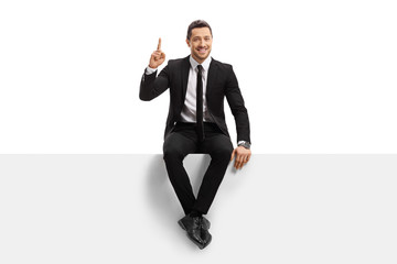 Young man in a suit sitting on a panel and pointing upwards