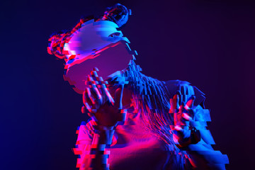 Woman is using virtual reality headset. Neon light studio portrait. Image with glitch effect.