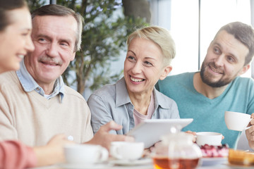 Group of people smiling and talking to each other while drinking tea together at the table