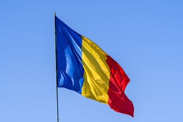 Romanian national flag blowing in the wind in direct sunlight towards clear blue sky
