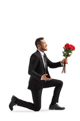 Young handsome man kneeling with a bunch of red roses