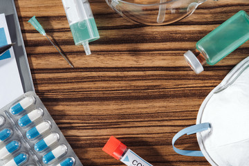 Medical still life. Wooden doctor desk background, horizontal medical concept copy space. Flat lay composition with siringe, needle, mask, pills, medical tube and bottle, patient form. COVID-19.