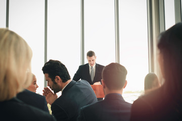 Group of business people sitting on conference together listening to the speaker giving a speech in the meeting room seminar, successful businessman sharing experiences