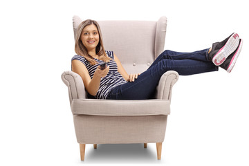 Young woman sitting in a cosy armchair and holding a remote control