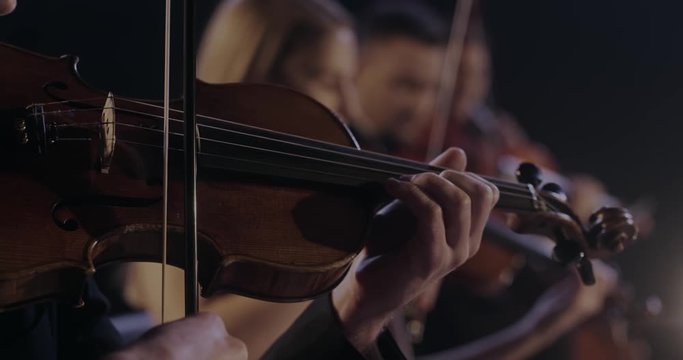 Close up of violin in hands of Caucasian man while he performing in classical orchestra. Male violinist playing on instrument at concert. Virtuoso concept.