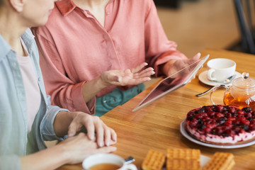 Fototapeta na wymiar Close-up of two women using digital tablet while sitting at the table and drinking tea with fruit cake