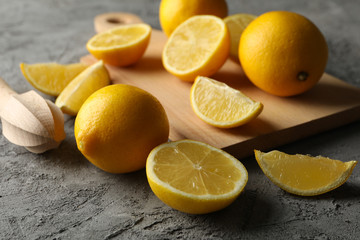 Board, lemons and juicer on gray background. Ripe fruit
