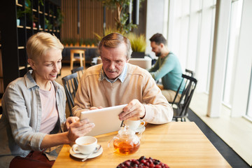 Fototapeta na wymiar Mature couple using digital tablet while drinking tea at the table in the restaurant
