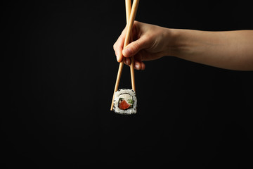 Female hand with chopsticks hold sushi roll on black background. Japanese food © Atlas