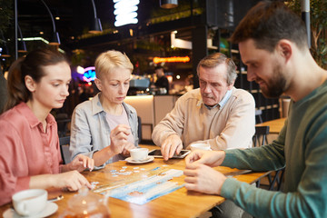 Mature parents with their adult children playing in board game together they collecting puzzle at the table