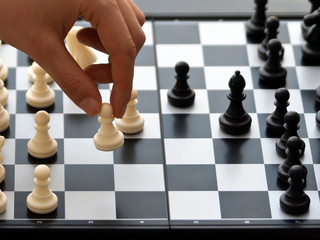 hand moving a white pawn on a chessboard during a chess game