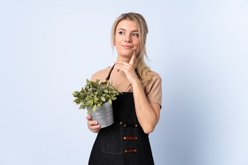 Blonde gardener woman holding a plant over isolated background thinking an idea