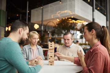 Family of four sitting at the table and playing in board game together in cafe