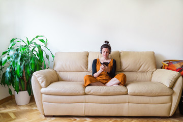 Panoramic view of casual woman calling a friend at home. Indoor lifestyle at spring time. Woman sit on the couch listening to music with headphones. Stay at home concept during quarantine isolation.