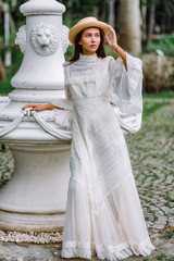 Fototapeta premium girl in a white dress and a straw hat walks in a beautiful park. bride in a vintage wedding dress in the garden.