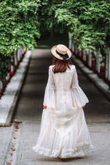 girl in a white dress and a straw hat walks in a beautiful park. bride in a vintage wedding dress...
