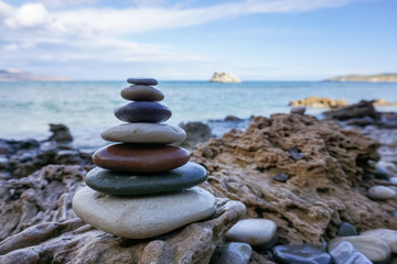 Fototapeta premium Pyramid of pebble stones on the sea beach. Concept of harmony and dzen in contrast to wavy sea and sharp rocks.
