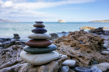 Pyramid of pebble stones on the sea beach. Concept of harmony and dzen in contrast to wavy sea and sharp rocks.