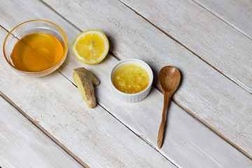 Mixture of grated ginger, lemon with honey in white bowl, spoon  on white wooden background