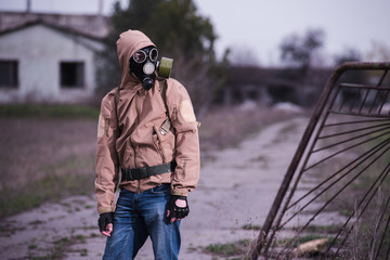 Man in gas mask, khaki jacket and blue jeans standing by the entrance to abandoned territory