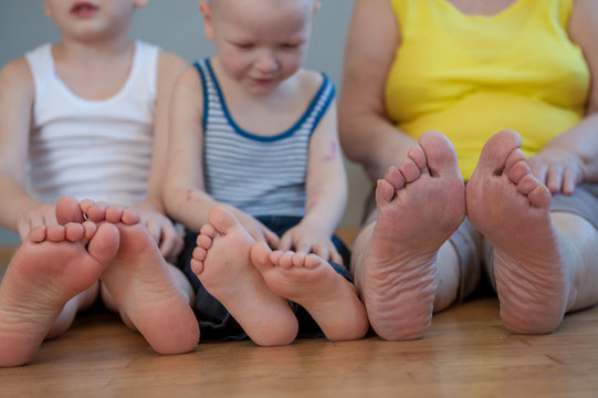 elderly woman in yellow T-shirt and sportswear sits on floor next to her grandchildren. Legs and feet close-up. Shallow depth of field