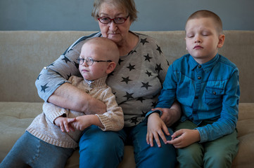 elderly woman sits and plays with her grandchildren on couch. Children love grandmother very much....